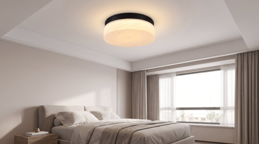 A cozy bedroom features a bed with white linens and a large window, brightly illuminated by a modern, warm-toned flush mount ceiling light.