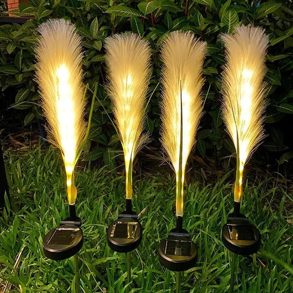 Four solar-powered feather lights on grass with greenery in the background