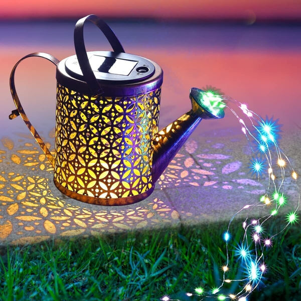 Decorative solar light shaped like a watering can with colorful string lights on grass.