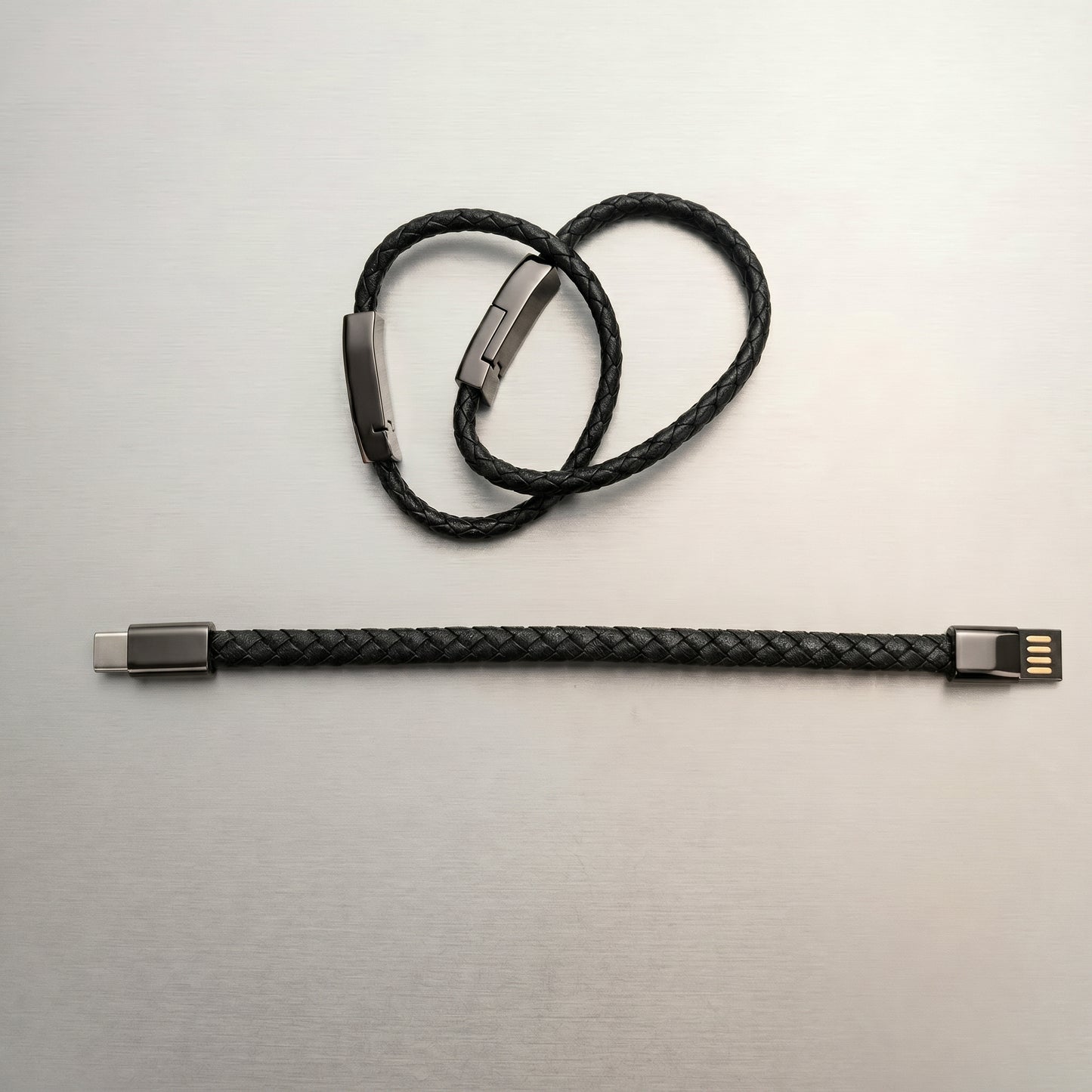 A black braided leather charging cable, displayed both as a stylish bracelet with a metallic clasp and straightened, revealing USB-A and USB-C connectors.