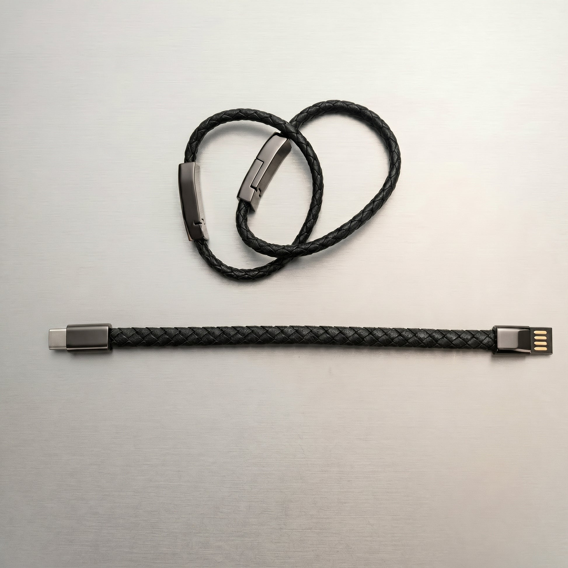 A black braided leather charging cable, displayed both as a stylish bracelet with a metallic clasp and straightened, revealing USB-A and USB-C connectors.