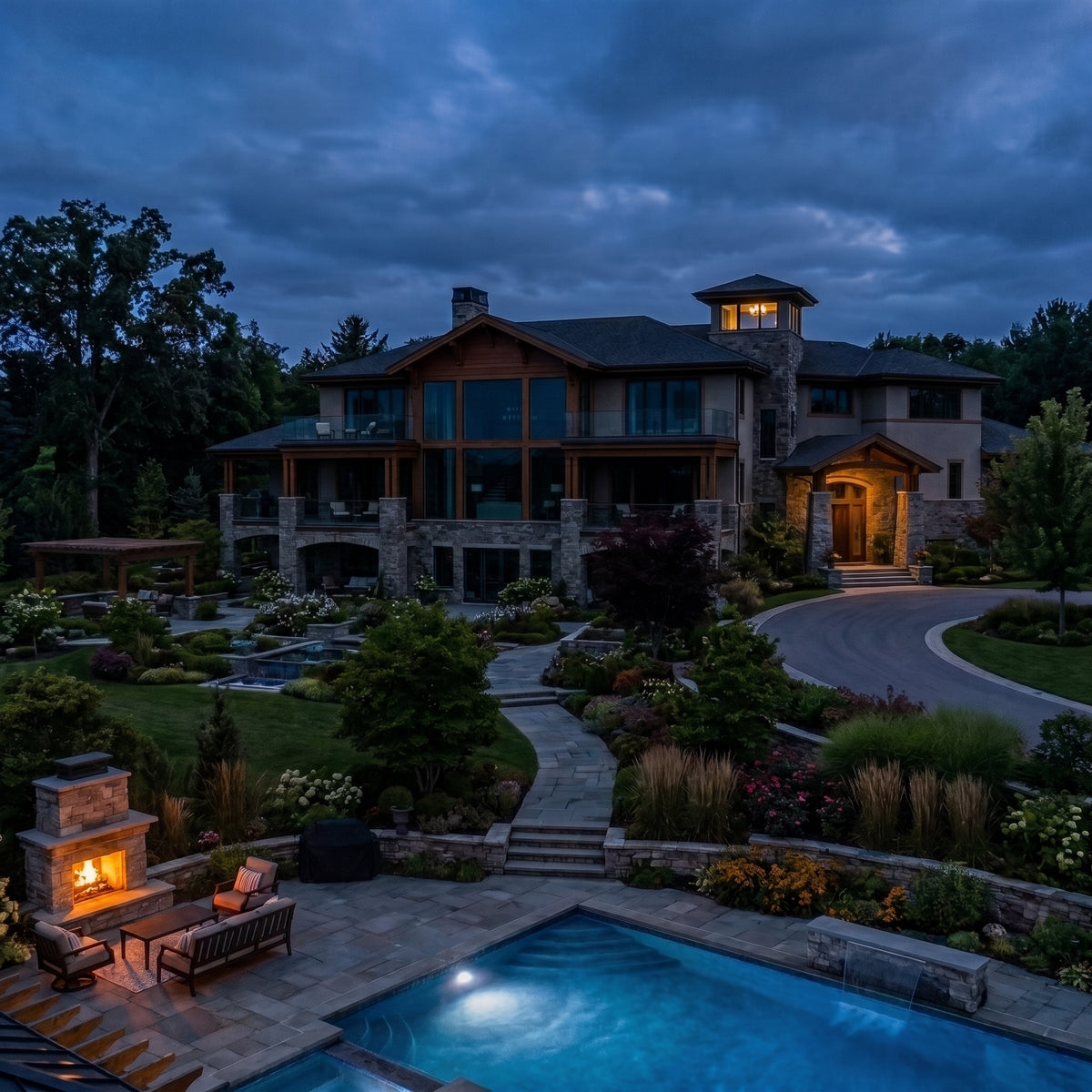The same large luxury estate at twilight before lighting installation, showing a dark, unlit house facade, hidden pathways, and unilluminated trees, with only minimal light from the pool and fireplace.