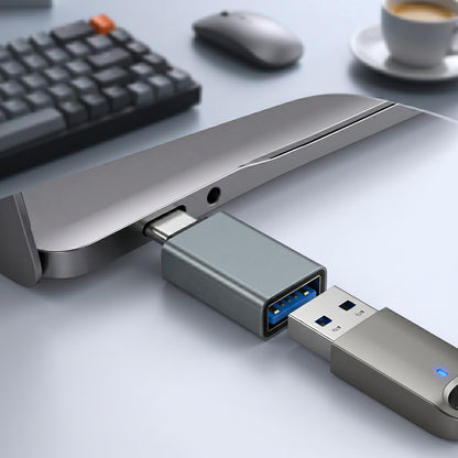 A blue-gray USB-C to USB-A adapter connects a device to a USB flash drive on a desk. The adapter facilitates connecting a USB-A peripheral to a USB-C port.