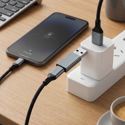 A gray USB adapter connects a phone, displaying "Charging," to a power strip. The phone charges via a braided cable on a wooden desk.