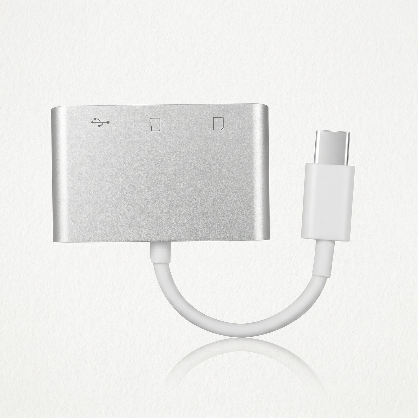 A silver USB-C hub adapter with a short white cable leading to a USB-C connector. Icons indicate USB and SD card reader functions on its face.