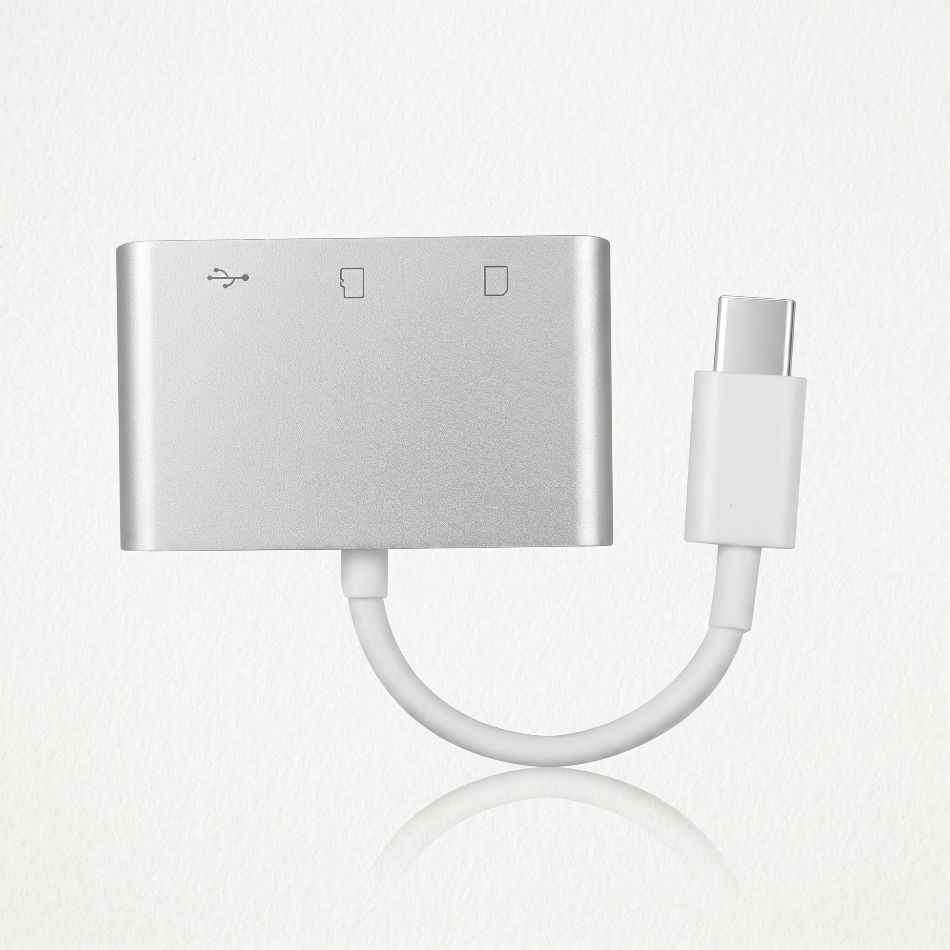 A silver USB-C hub adapter with a short white cable leading to a USB-C connector. Icons indicate USB and SD card reader functions on its face.