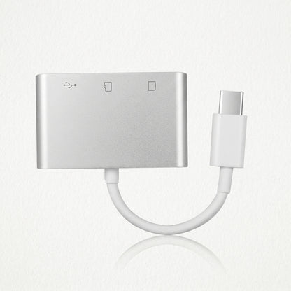 A silver USB-C hub adapter with a short white cable leading to a USB-C connector. Icons indicate USB and SD card reader functions on its face.