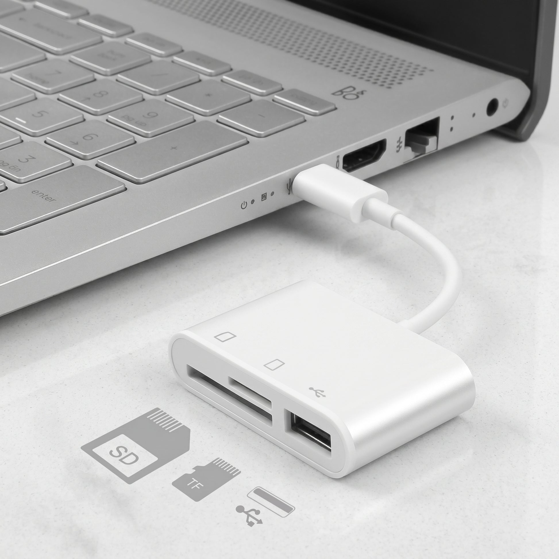 A white Zainzio 3-in-1 USB-C hub adapter, reading SD and TF cards, plugged into a silver laptop. Visible text: SD, TF.