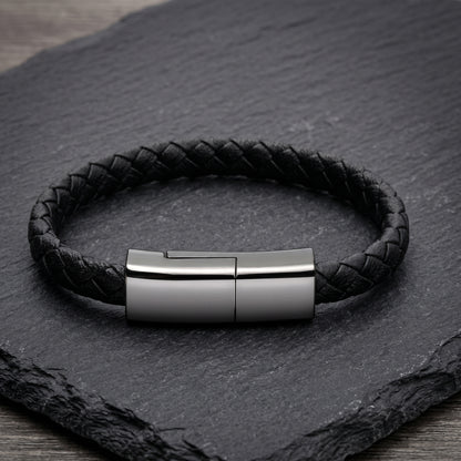 A black braided leather bracelet with a sleek, rectangular gunmetal clasp. This versatile accessory discretely functions as a USB-C charging cable.