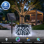 Solar-powered string lights shown in a real backyard setting with a tree wrapped in warm white lights, a coiled roll of black string lights in the foreground, a solar panel stake, and a patio pergola in the background. A ZAINZIO logo appears in the top left, and feature icons along the bottom.
