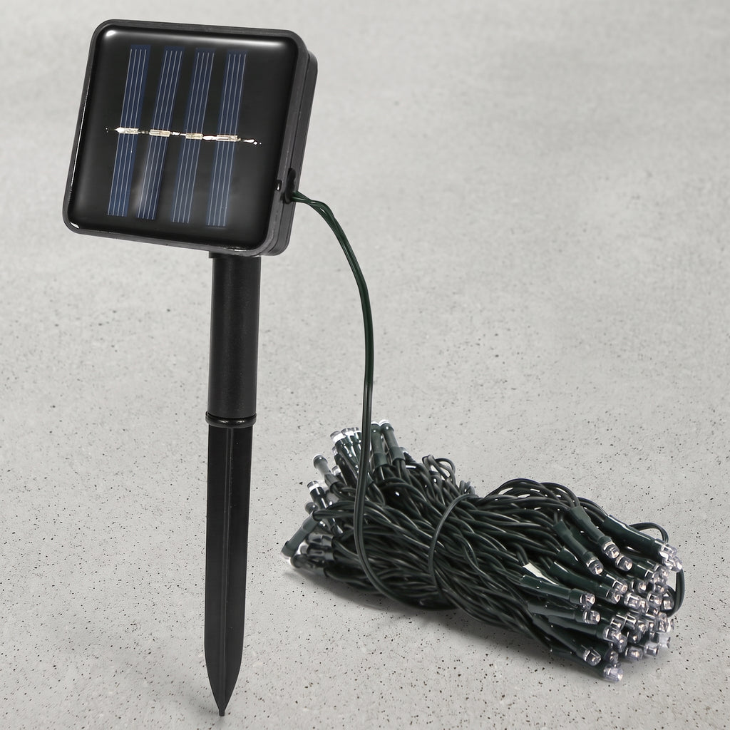 Solar-powered garden string lights with a black rectangular solar panel on a stake and a coiled bundle of green wire lights on a gray textured background.