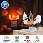 A Zainzio Halloween night light plug-in featuring two white cartoon ghosts sitting on a log and playing with a small flame. The main product is shown in the foreground on a tabletop, with a smaller inset view of the same product plugged into an outlet in the background.