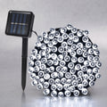 A solar-powered LED light string with a black stake-mounted solar panel on the left and a dense cluster of clear dome-shaped LED bulbs on the right, set against a neutral gray background.