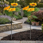 Two solar-powered artificial sunflower garden lights planted in a stone garden bed, with yellow flowers, green leaves, and black solar panels visible.