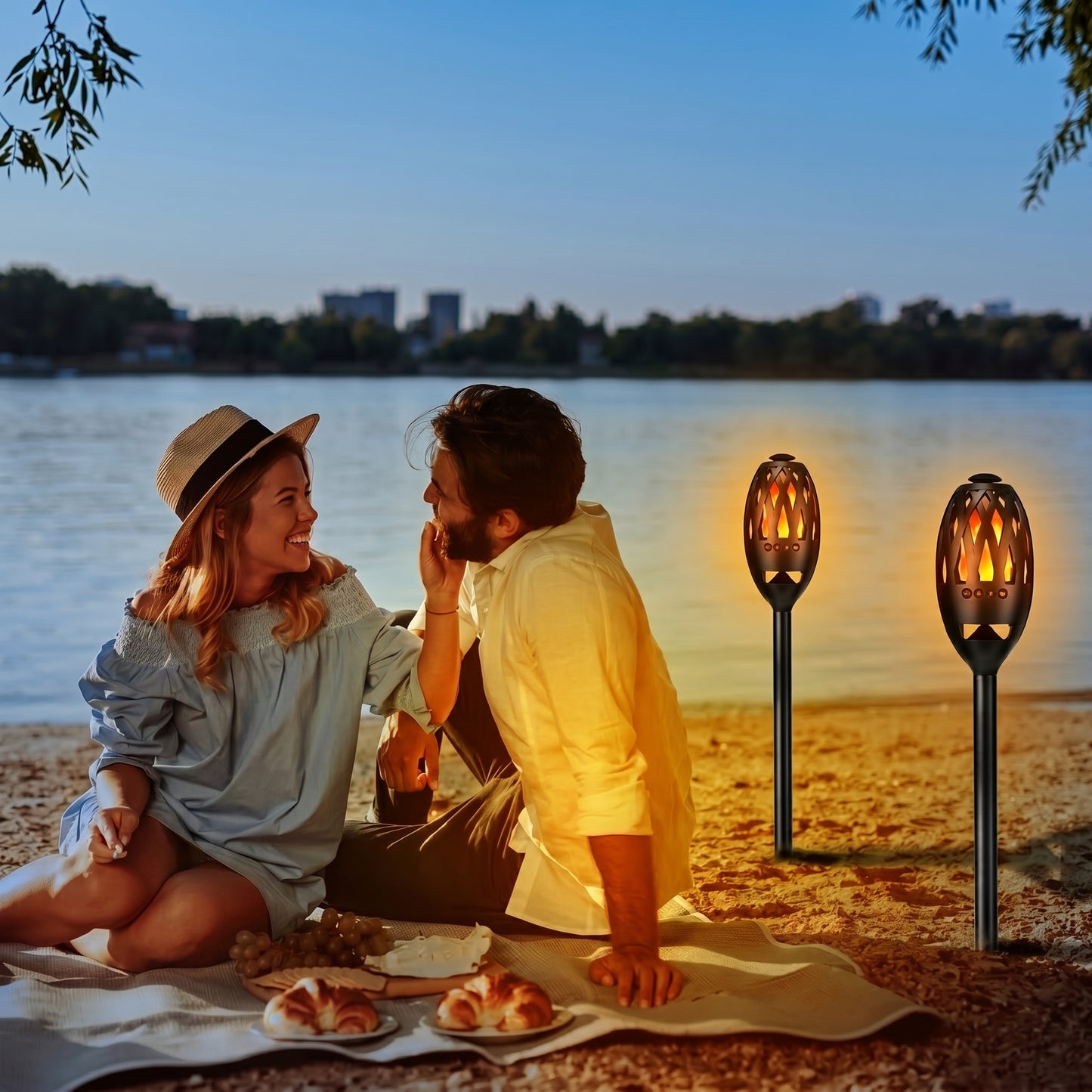 A couple enjoys a romantic beach picnic at sunset, illuminated by two glowing Zainzio LED flame torches. This scene highlights the product's ambiance for outdoor use.