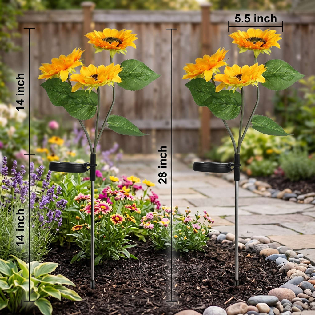 Two solar-powered artificial sunflower garden stakes shown in a landscaped garden bed with size annotations: one labeled 14 inch tall by 14 inch wide, and another 28 inch tall by 5.5 inch wide.