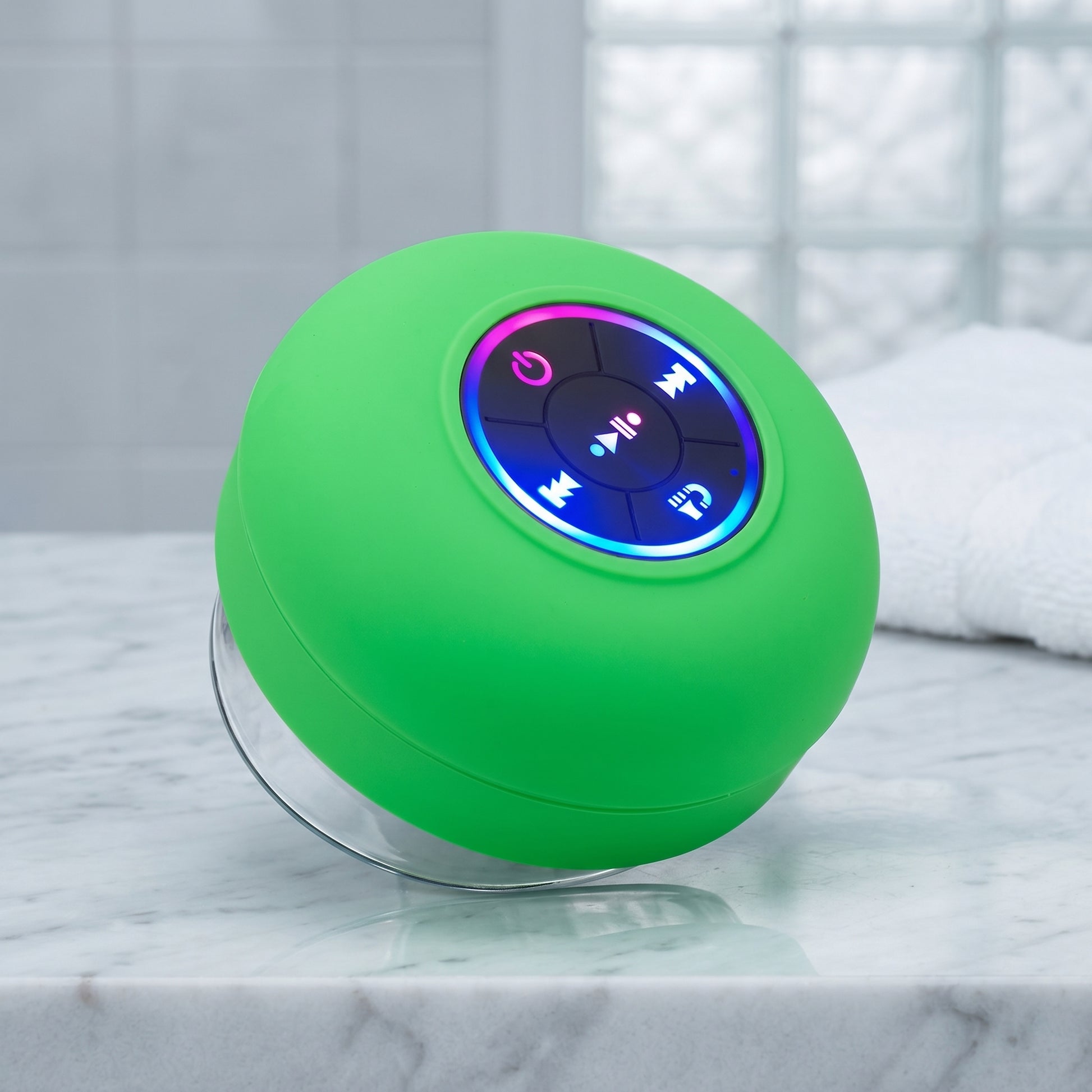 A vibrant green waterproof Bluetooth speaker with an LED-lit control panel and a clear suction cup base, resting on a white marble counter. The speaker's lights glow blue, pink, and purple.