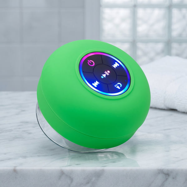 A vibrant green waterproof Bluetooth speaker with an LED-lit control panel and a clear suction cup base, resting on a white marble counter. The speaker's lights glow blue, pink, and purple.