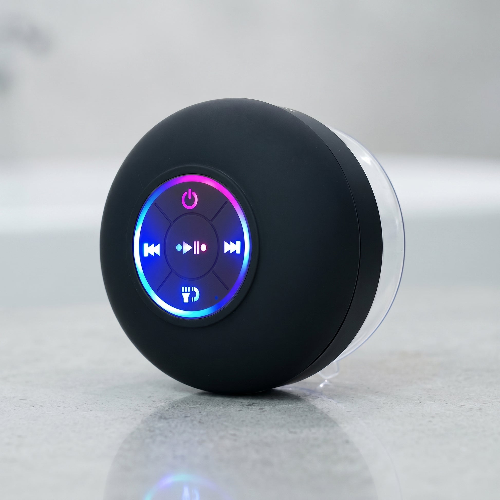 A black, round waterproof Bluetooth speaker is shown. It features a central control panel with glowing blue and pink LED buttons for power, playback, and calls.