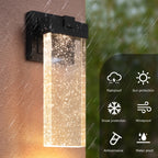 A wall-mounted outdoor light fixture with a black metal bracket and a clear rectangular glass shade filled with glowing warm light particles. The left half shows the fixture mounted on a wall in rain, while the right half shows feature icons for rainproof, sun protection, snow protection, windproof, anticorrosive, and water proof over a blurred green background.