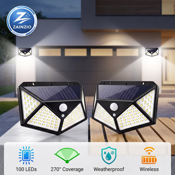 Two black solar-powered outdoor security light fixtures shown on a wooden deck in front of a house, with beams of light projecting outward. The image includes a ZAINZIO brand logo in the top-left corner and feature icons at the bottom highlighting 100 LEDs, 270-degree coverage, weatherproof design, and wireless operation.