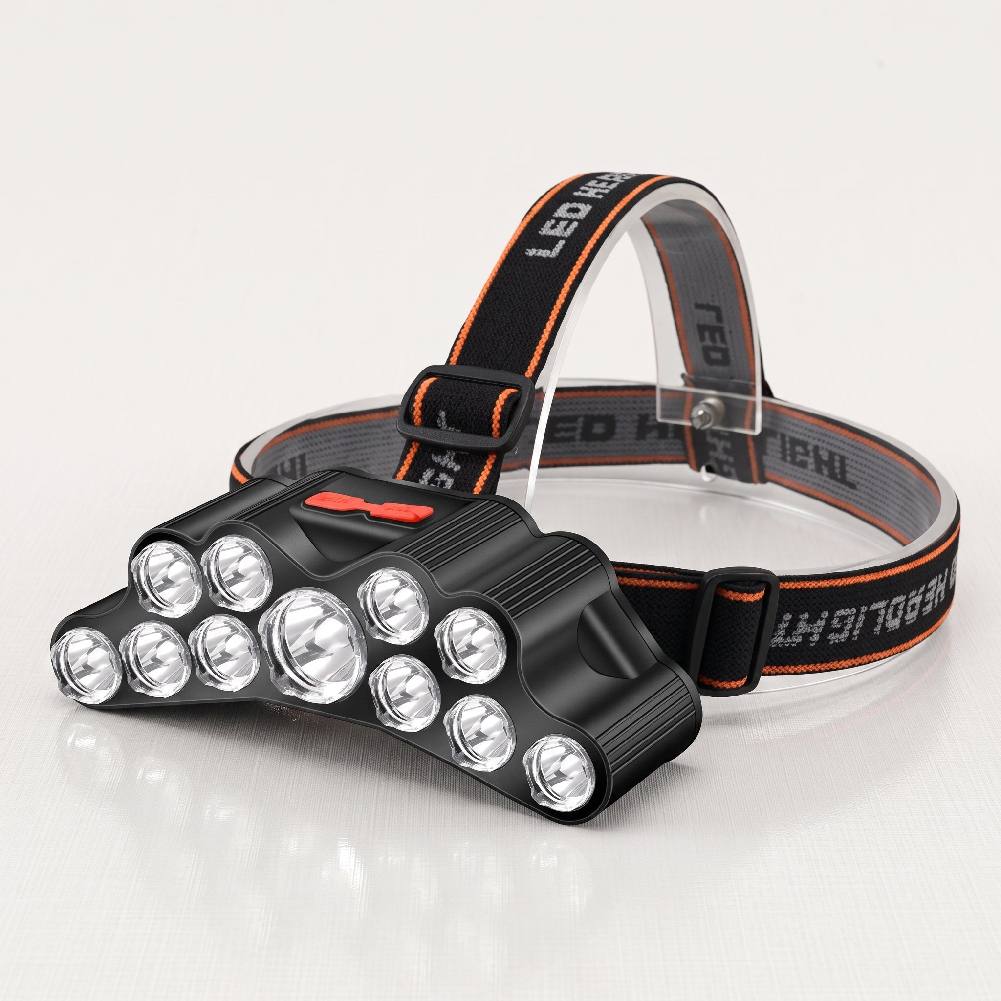 A black LED headlamp with multiple clear lenses and an adjustable black and orange head strap, shown on a clean white background.