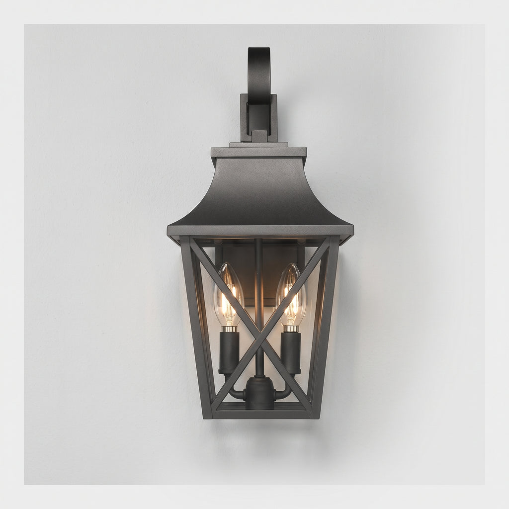 A dark charcoal outdoor wall sconce with a lantern-style frame, two visible warm Edison bulbs, and a curved mounting bracket at the top, shown against a light gray background.
