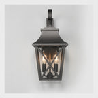 A dark charcoal outdoor wall sconce with a lantern-style frame, two visible warm Edison bulbs, and a curved mounting bracket at the top, shown against a light gray background.