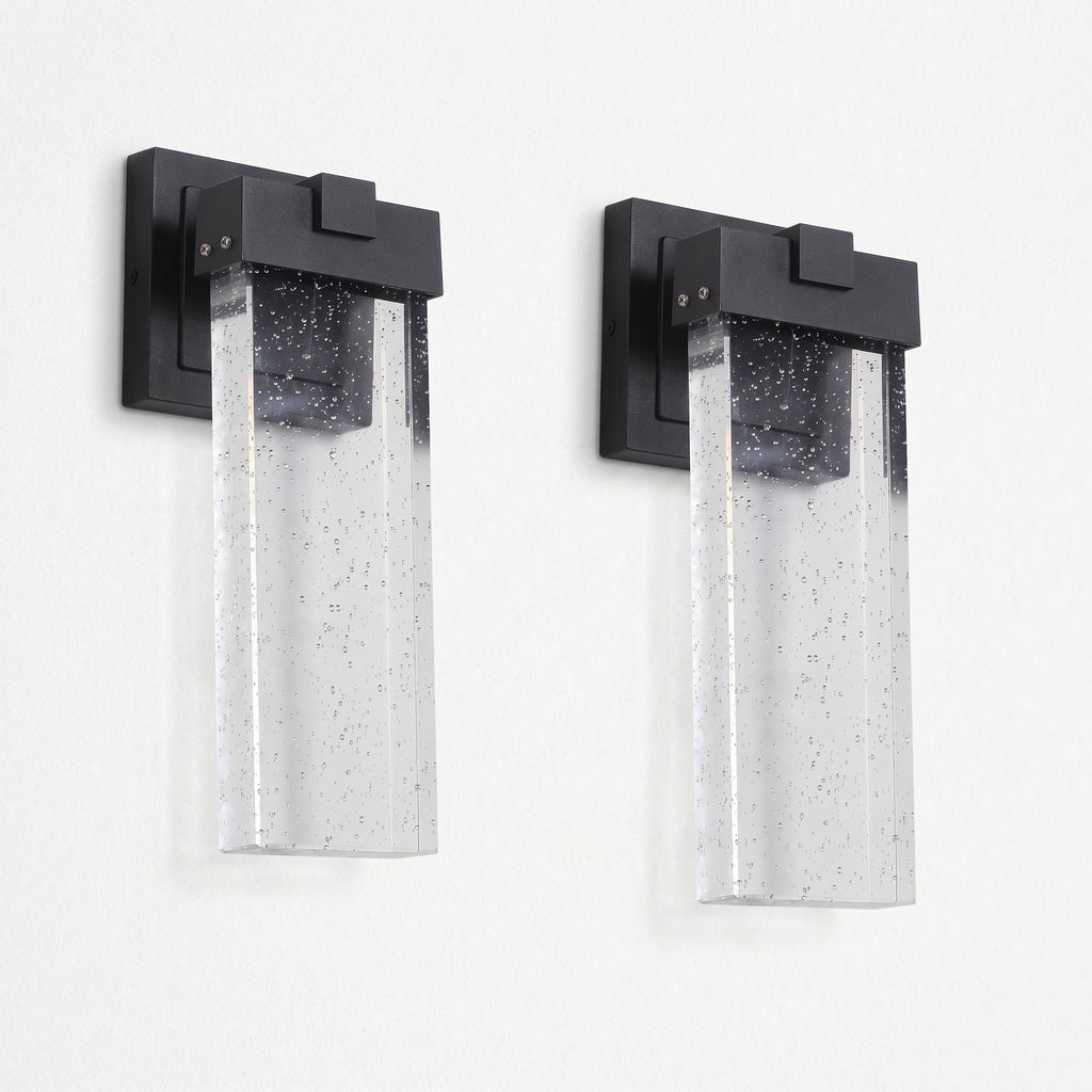 Two matching outdoor wall sconces with matte black rectangular mounts and clear seeded glass shades, shown side by side against a plain white wall.