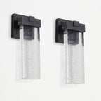 Two matching outdoor wall sconces with matte black rectangular mounts and clear seeded glass shades, shown side by side against a plain white wall.