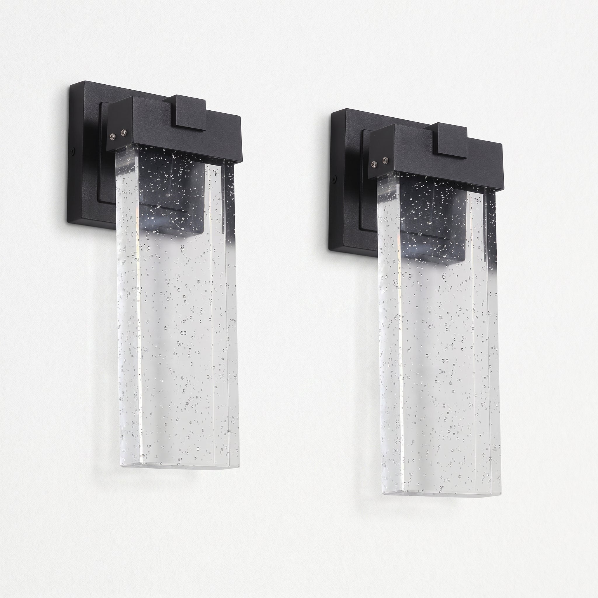 Two matching outdoor wall sconces with matte black rectangular mounts and clear seeded glass shades, shown side by side against a plain white wall.