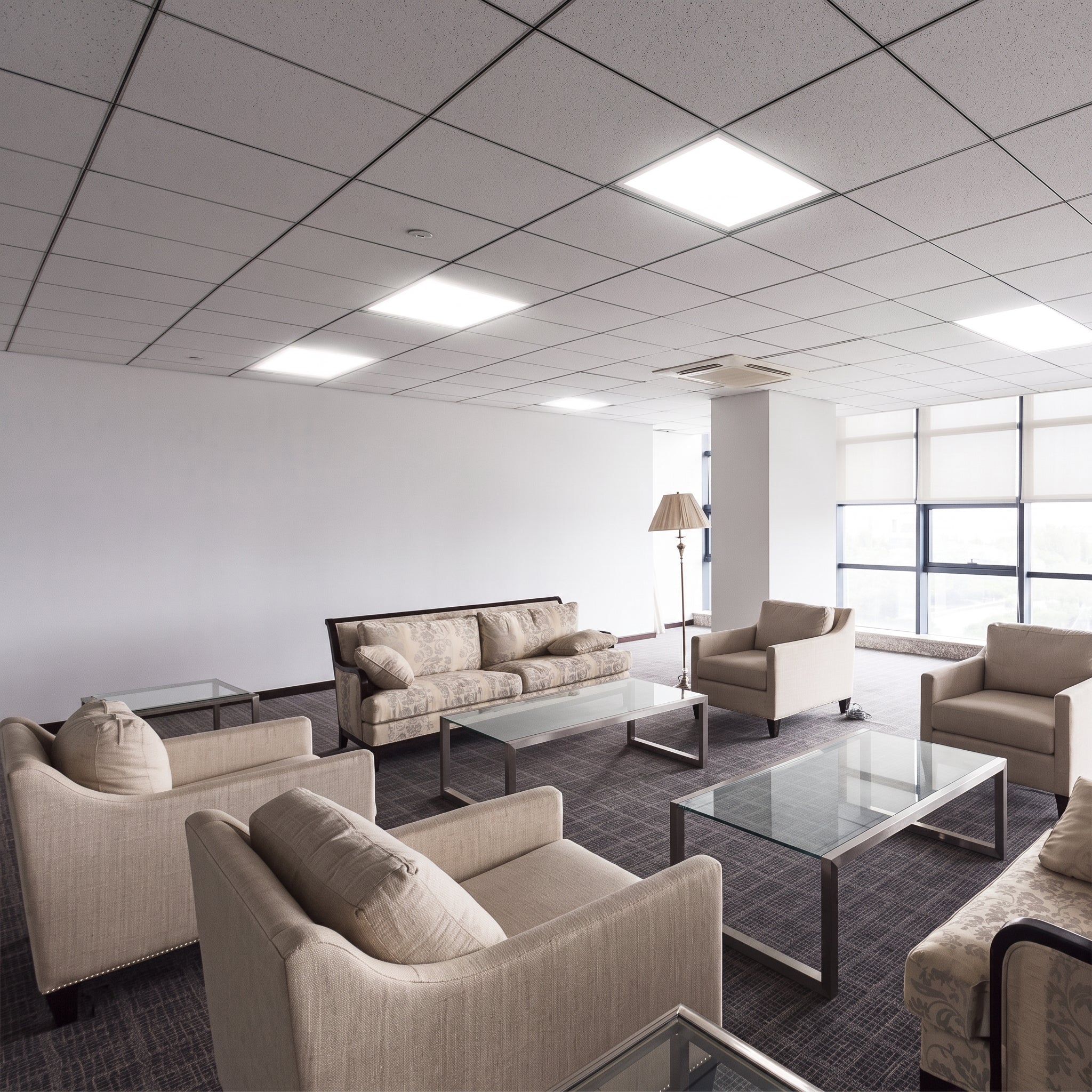 Modern office waiting area with beige sofas and glass coffee tables.