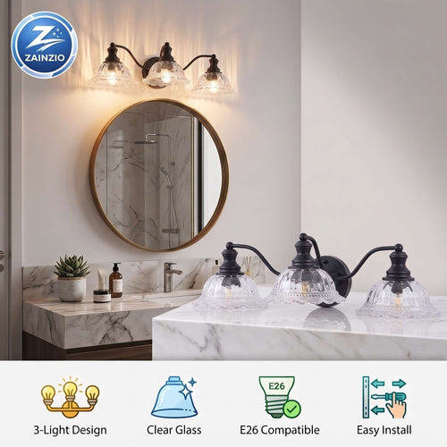 A wall-mounted three-light bathroom vanity fixture with clear glass shades and black metal arms, shown installed above a marble sink in a real bathroom setting. The image also includes a circular mirror, sconce, and feature icons at the bottom describing the product.