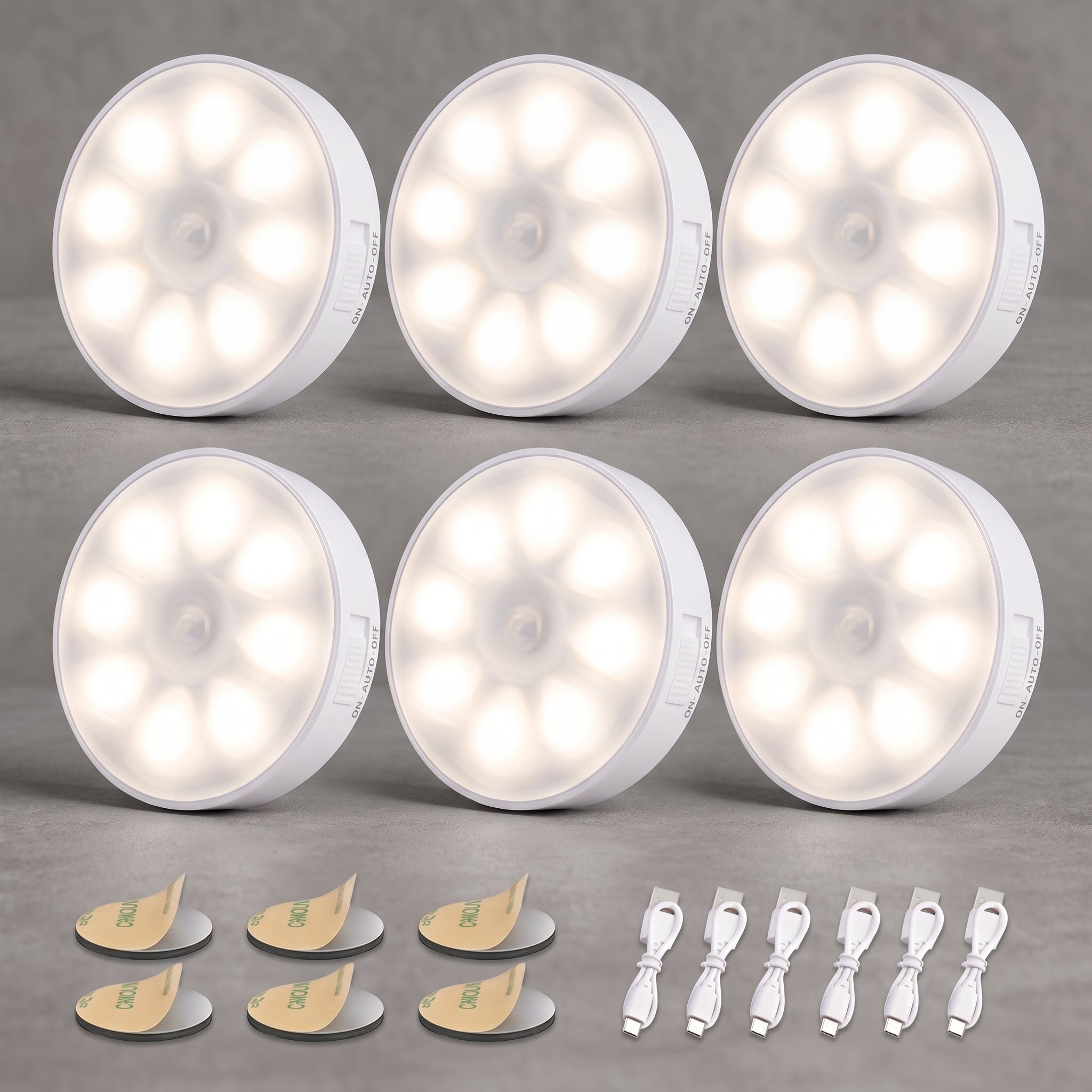 Six white round LED under-cabinet lights arranged in two rows on a gray background, with six adhesive pads and six USB charging cables shown below.