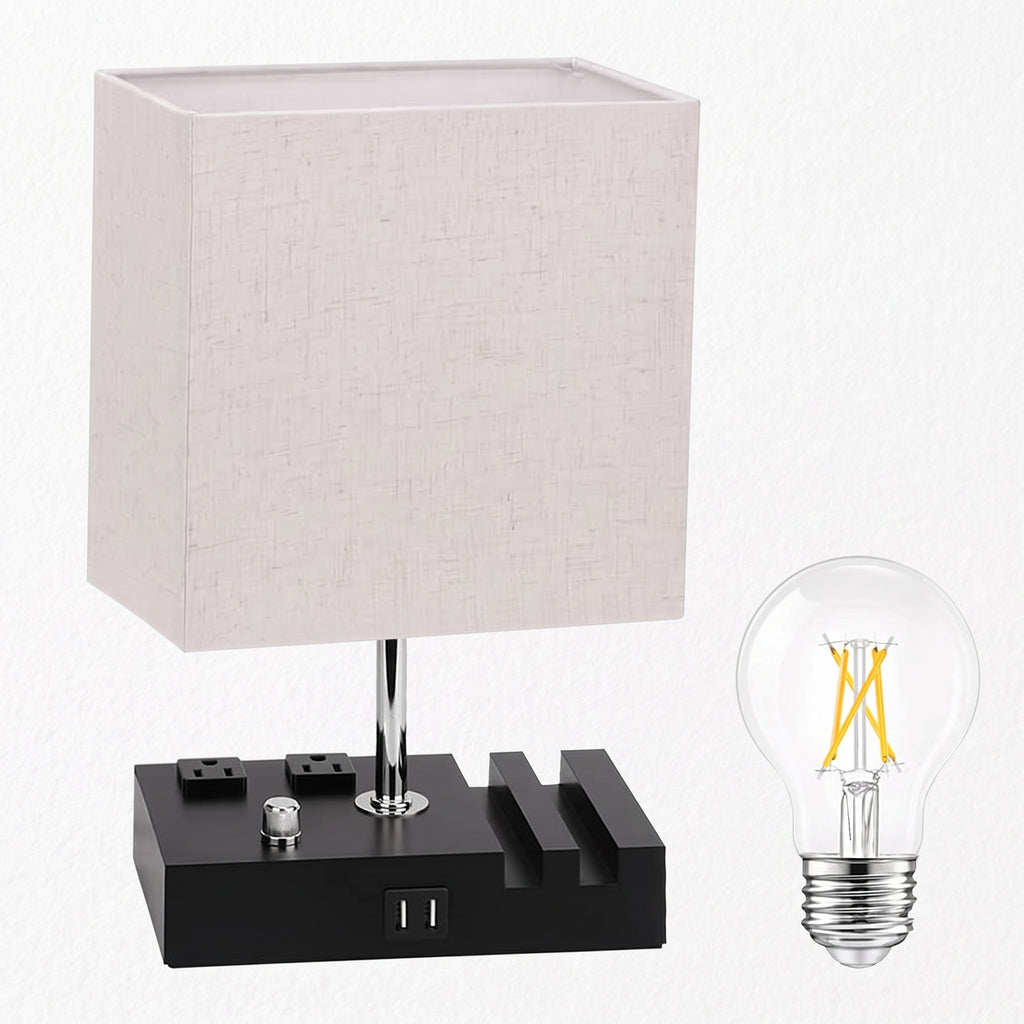 A modern table lamp with a square off-white linen shade, a black power bank-style base with built-in outlets, and a separate clear LED filament bulb shown beside it on a white background.