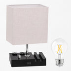 A modern table lamp with a square off-white linen shade, a black power bank-style base with built-in outlets, and a separate clear LED filament bulb shown beside it on a white background.