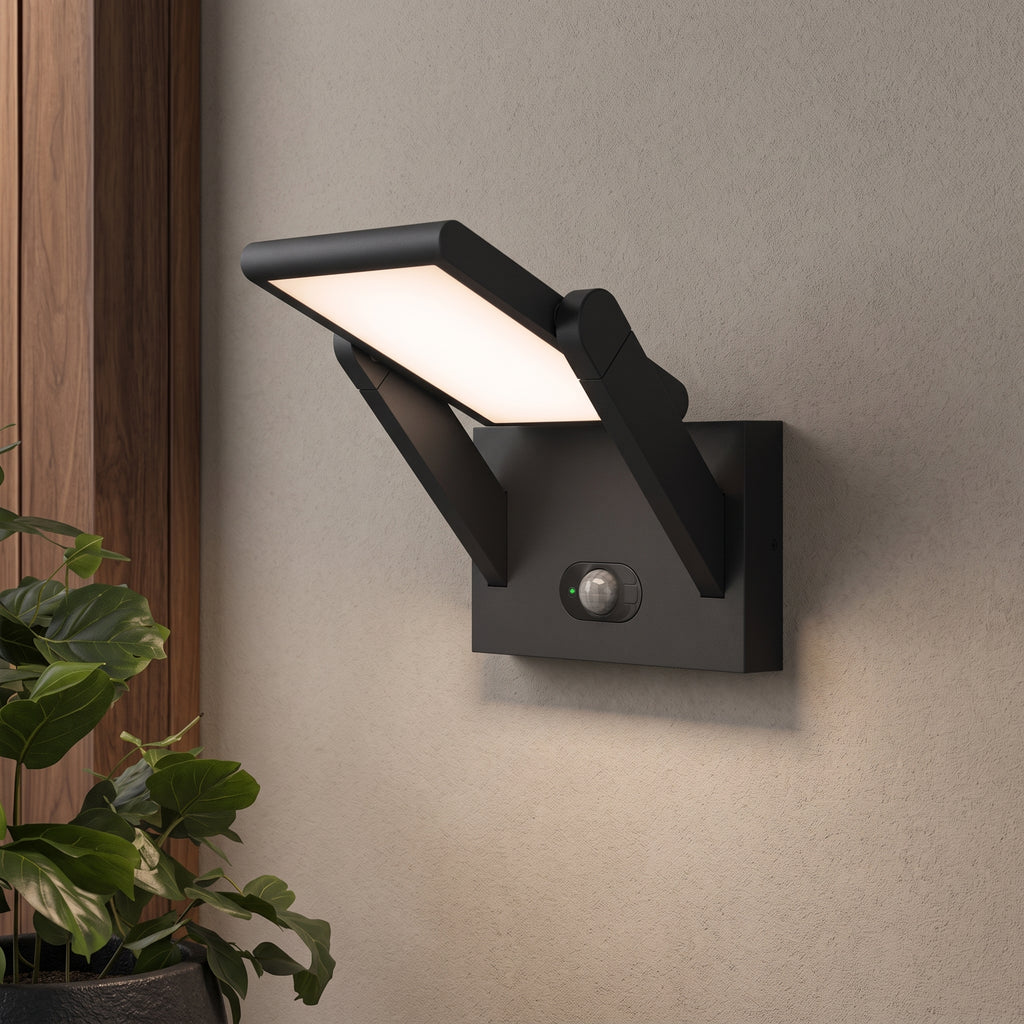 A modern black outdoor wall sconce with a built-in motion sensor, mounted on a textured beige wall next to a wooden panel and a potted green plant.