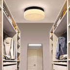 A modern flush-mount ceiling light with a round white textured glass shade and a black metal rim, installed in a walk-in closet.