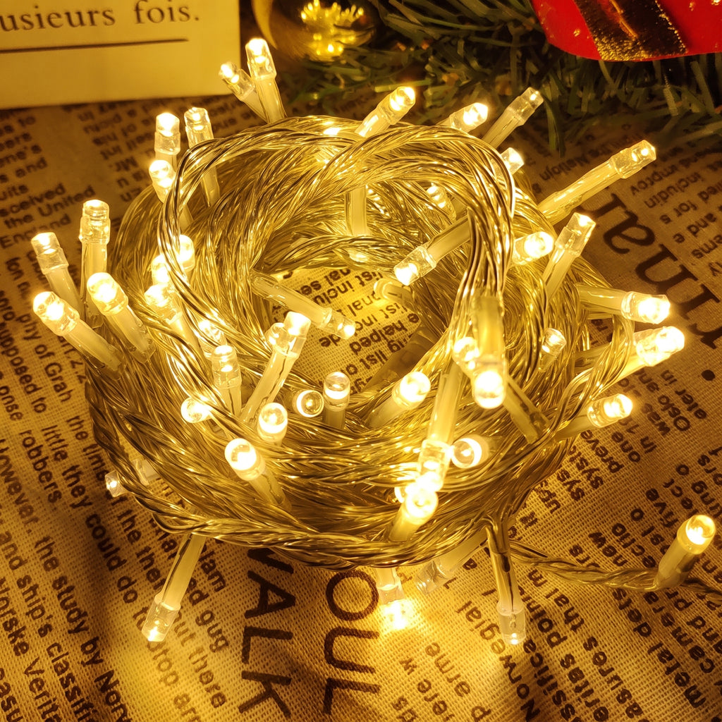 Warm white LED fairy string lights coiled on a printed fabric surface, glowing brightly with a golden-yellow cast.