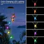 Color-changing hummingbird wind chimes hanging outdoors at night by the ocean, with a large demonstration scene on the left and six smaller color options on the right.