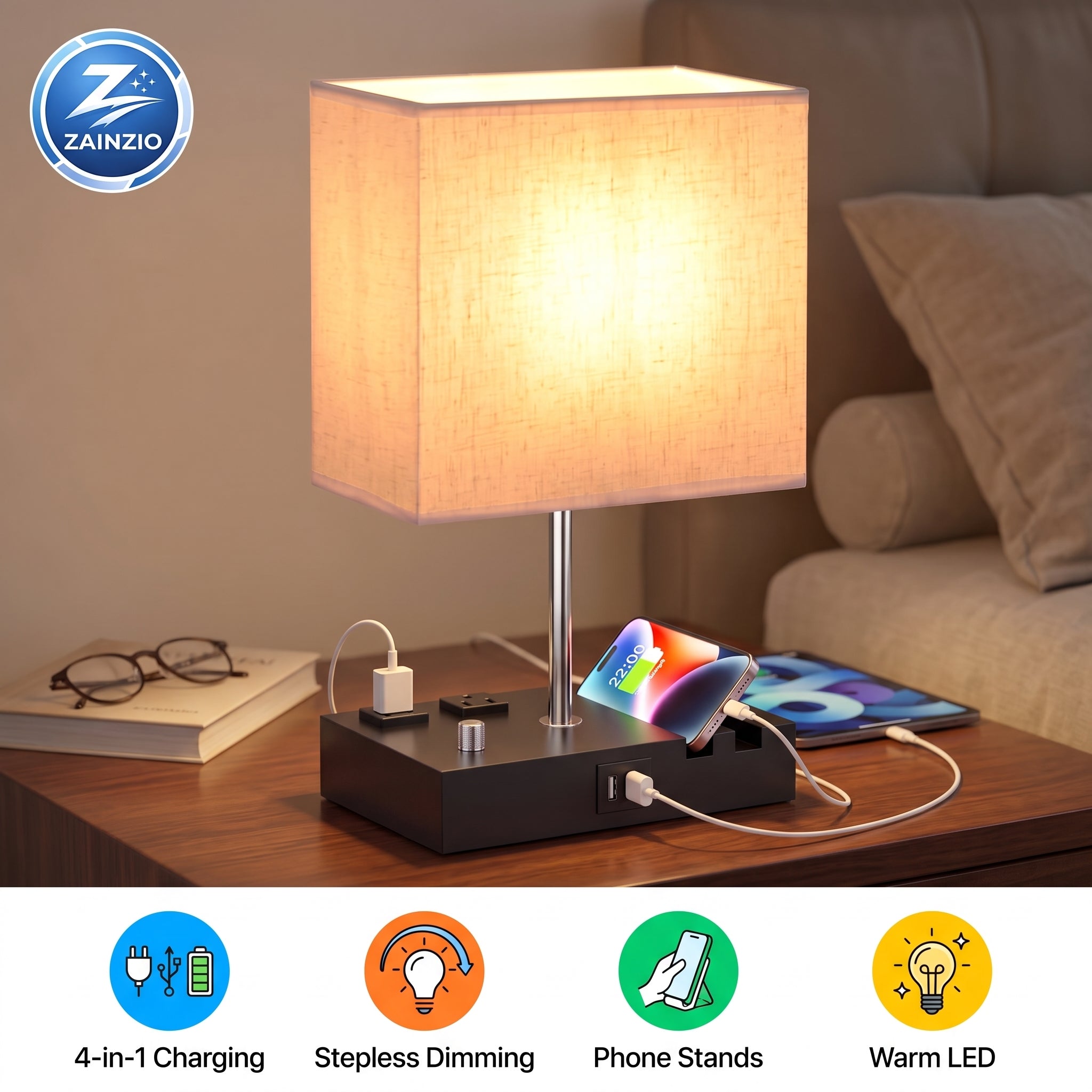 A ZAINZIO 4-in-1 bedside table lamp with a warm white fabric shade, a slim silver metal stem, and a black charging base. The lamp is shown illuminated on a wooden nightstand, with a smartphone resting on its charging platform and other charging accessories plugged into the side.