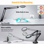 Black adjustable desk lamp with stand and clip mounting, shown on a white desk with text highlighting wide field of view, eye-friendly use, and more stability. Small inset diagrams explain eye focus and arm stability.