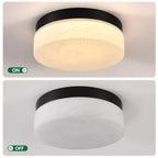 A round flush-mount ceiling light shown in two states: illuminated with a warm white glow in the top panel, and unlit in the bottom panel. The fixture has a black top band and a frosted white glass diffuser.