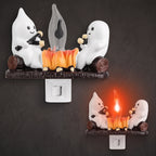 Two ghost-shaped night lights shown on a dark textured background, one lit and one unlit, each featuring white ghosts sitting on logs with a glowing orange campfire between them.