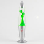 A classic lava lamp with a clear glass bulb filled with bright neon green liquid and bubbles, set in a metallic silver base with a red circular warning label.