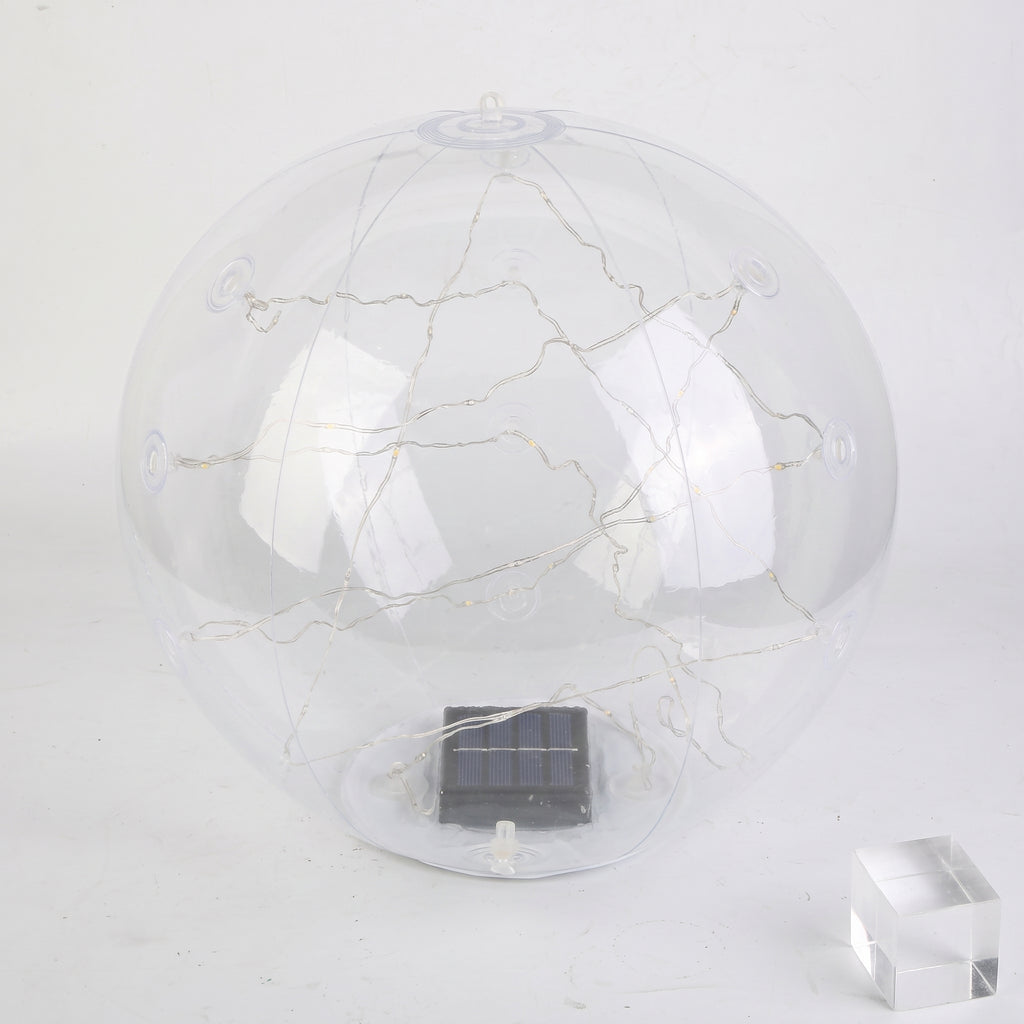 A clear spherical solar globe lamp with internal warm white string lights and a small dark solar panel at the base, shown on a plain light background with a small transparent block prop.