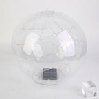 A clear spherical solar globe lamp with internal warm white string lights and a small dark solar panel at the base, shown on a plain light background with a small transparent block prop.