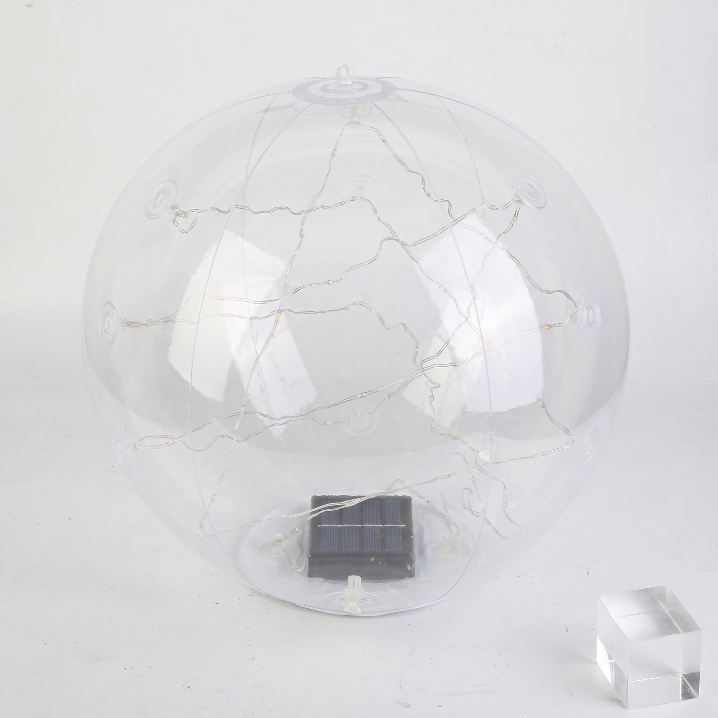A clear spherical solar globe lamp with internal warm white string lights and a small dark solar panel at the base, shown on a plain light background with a small transparent block prop.