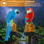 Two LED solar light parrot sculptures perched on rock-shaped bases, shown outdoors in the rain with a stormy sky and green foliage in the background. An orange banner at the top highlights waterproof and heatproof features.
