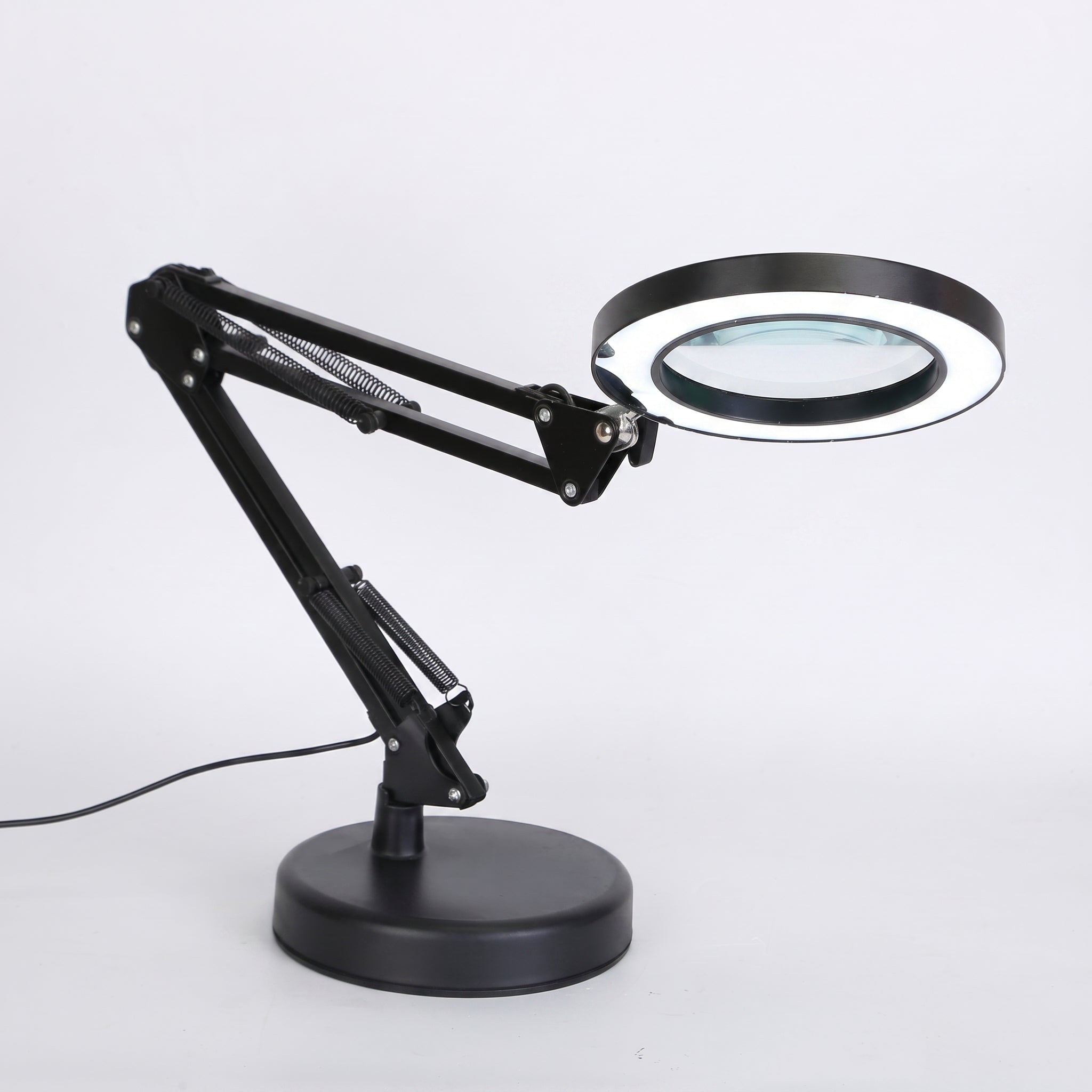 A black adjustable desk magnifier lamp with a circular LED ring light and a large viewing lens, mounted on a round base with a power cord, shown against a plain white background.